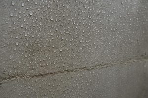 Moisture beading on a grey concrete basement wall surface