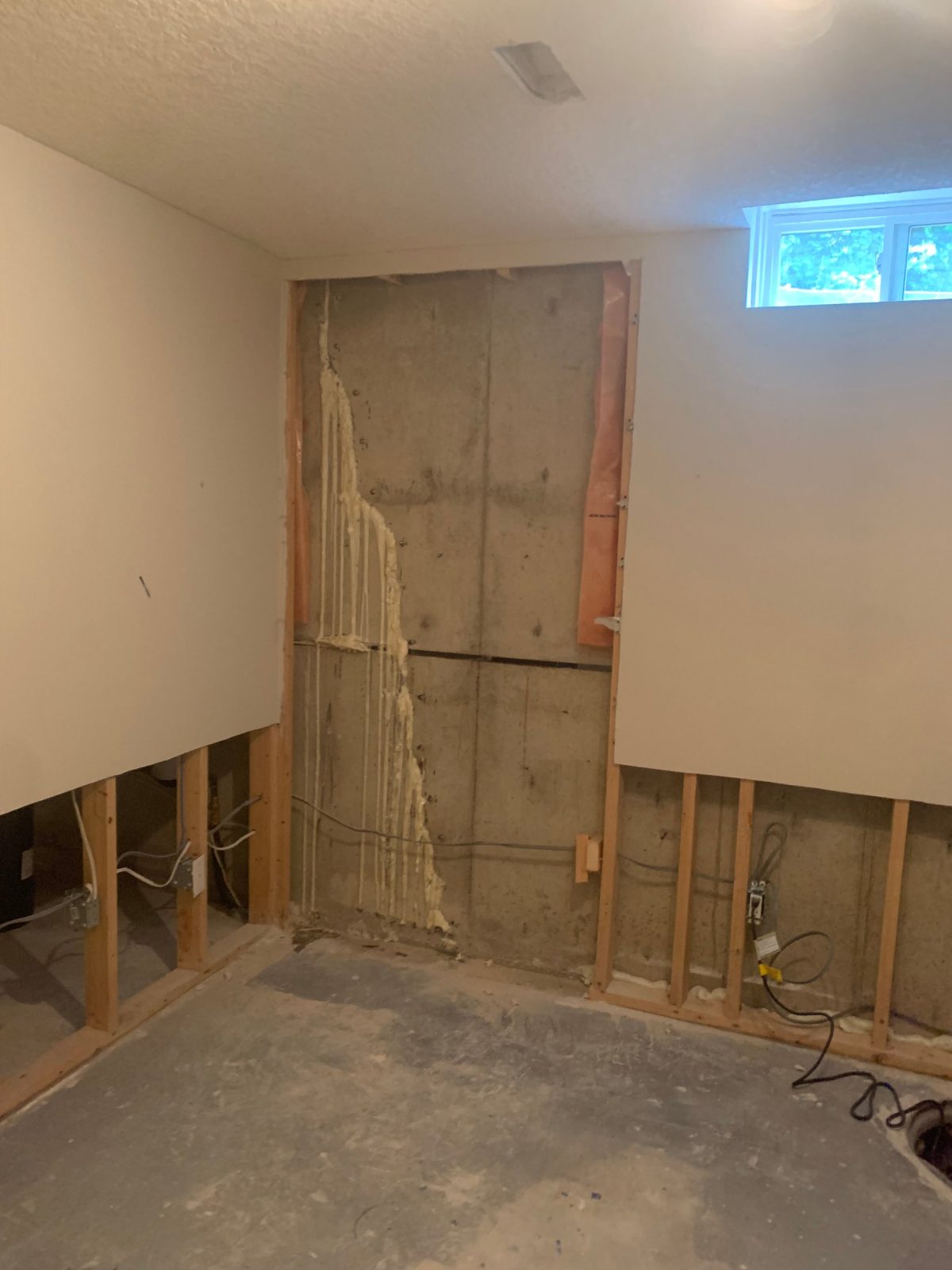 Finished basement with a section of drywall removed, showing a foundation crack sealed with polyurethane injection