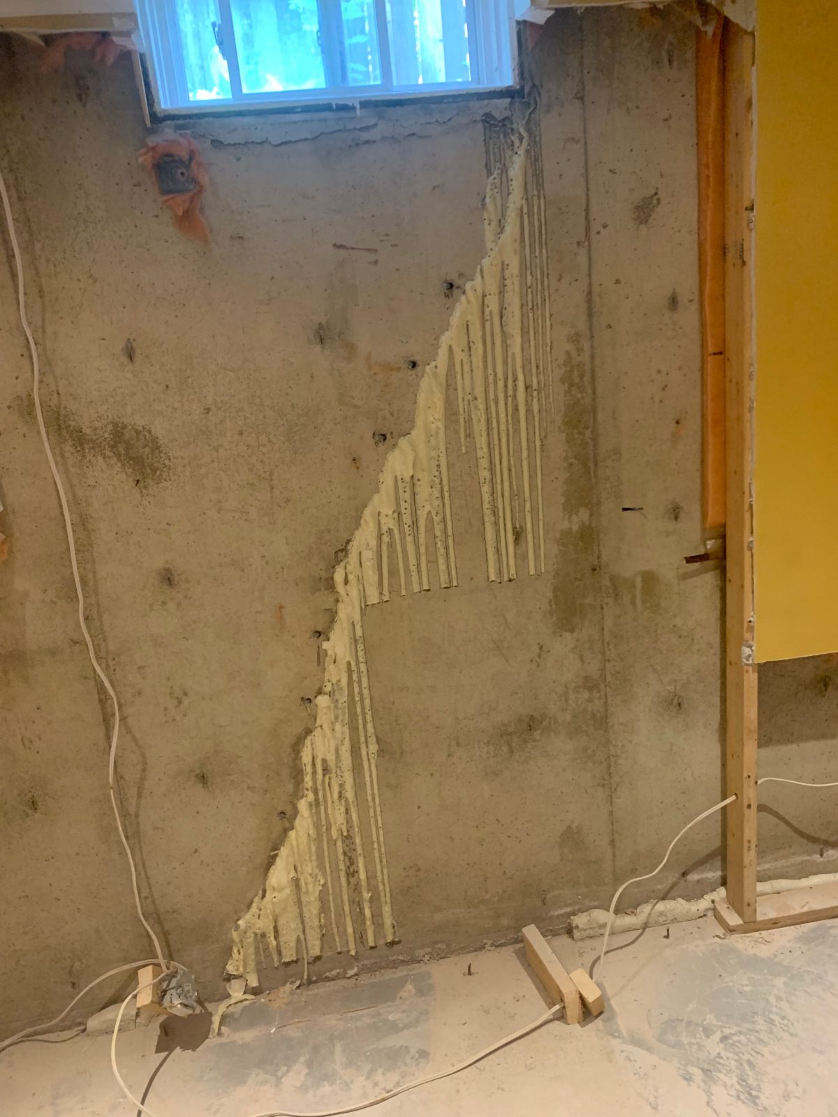 Diagonal foundation crack below a basement window after polyurethane crack injection, with cured resin along the crack line