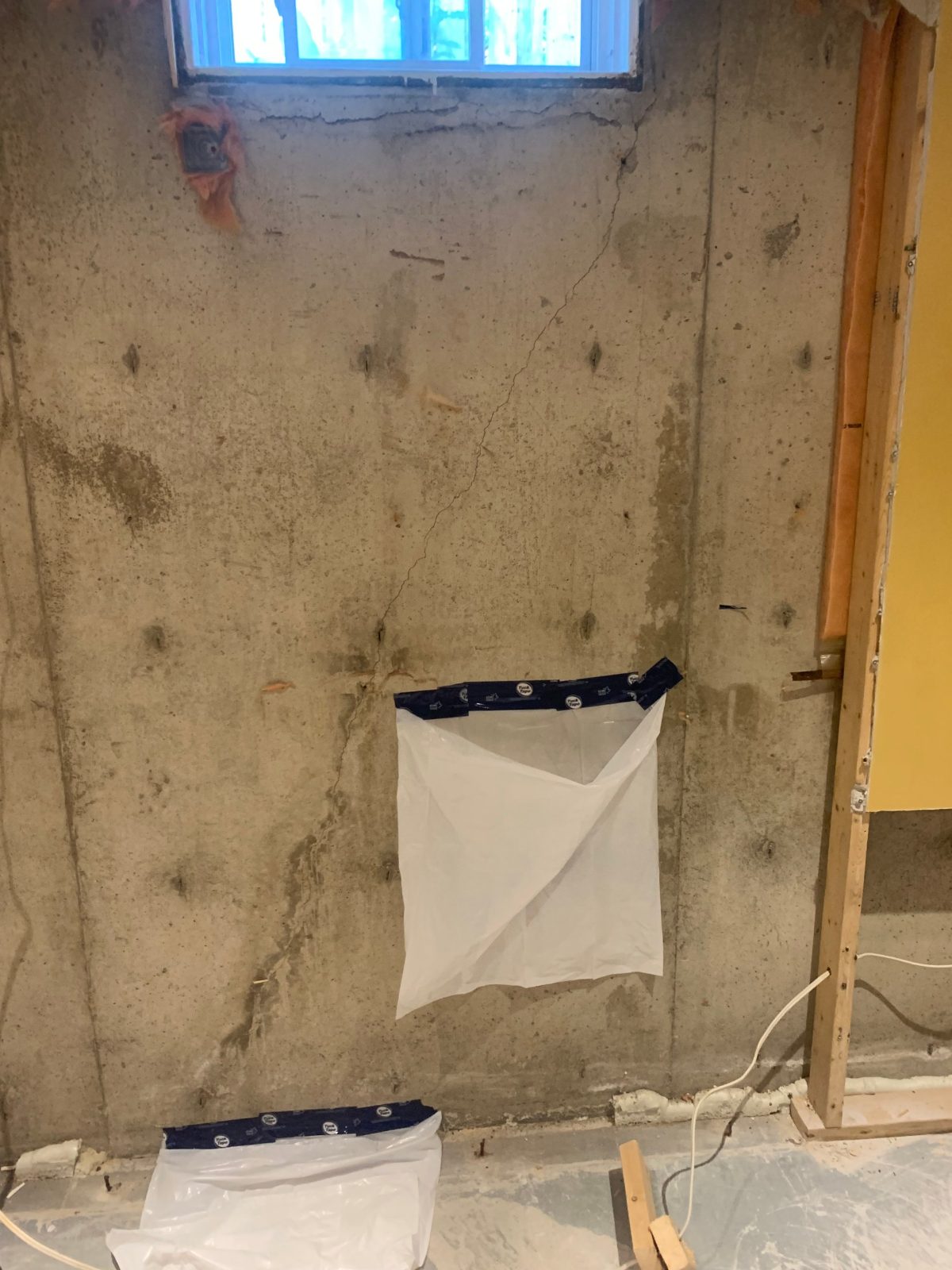 Diagonal crack running down from a basement window corner in a poured concrete foundation wall, before crack injection