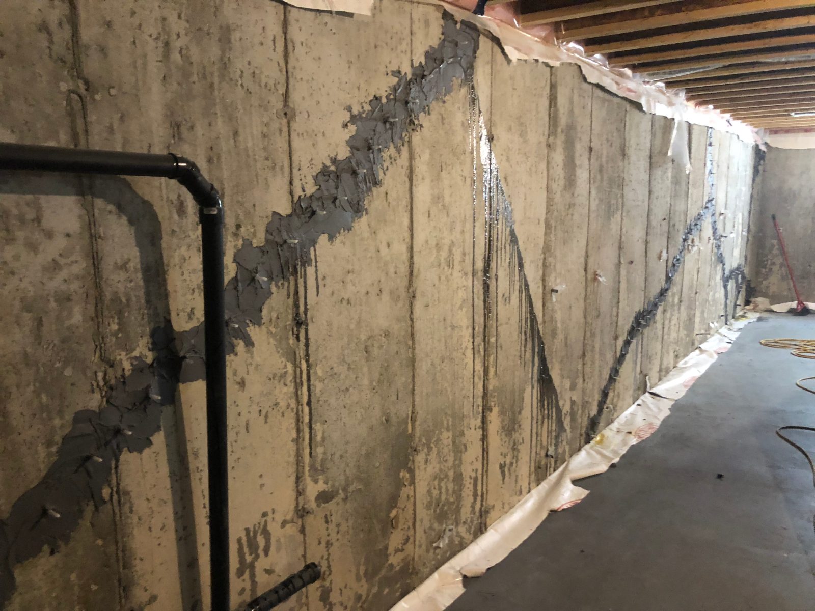 Long diagonal cracks along a poured concrete foundation wall sealed with grey epoxy paste and fitted with surface ports for epoxy crack injection