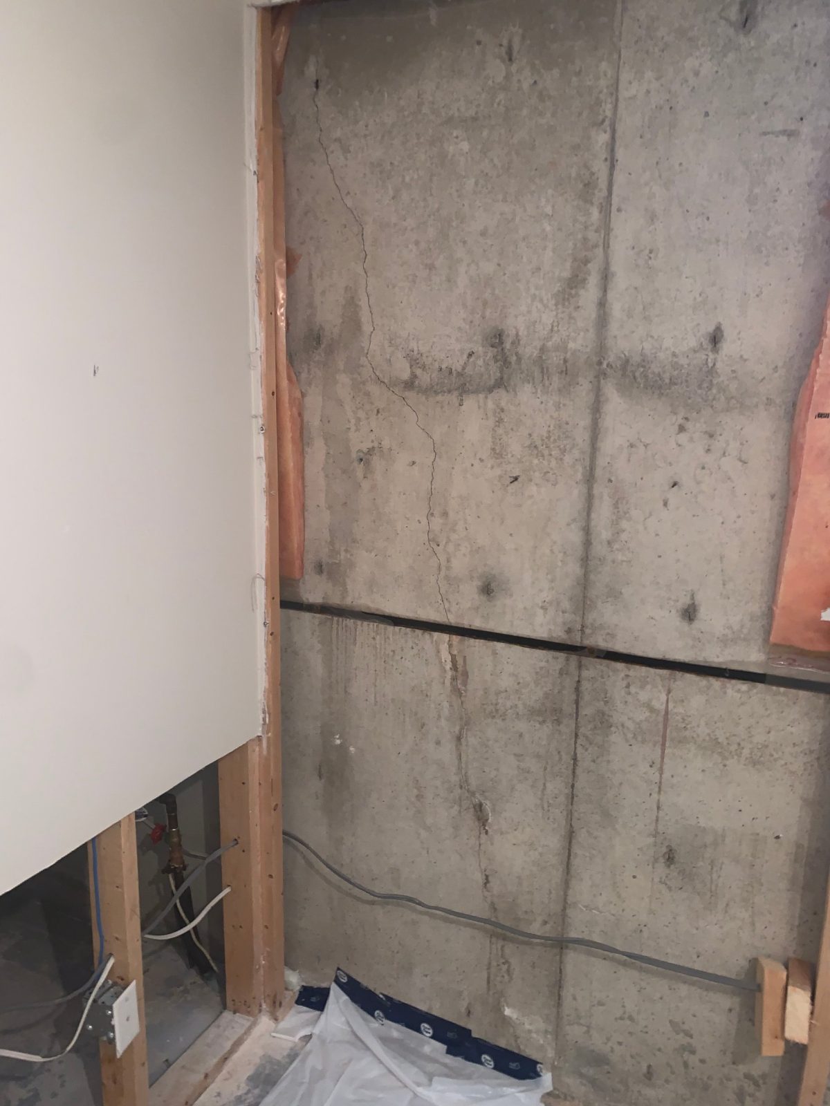 Crack in a poured concrete foundation wall exposed by a drywall cut-out in a finished basement, before crack injection