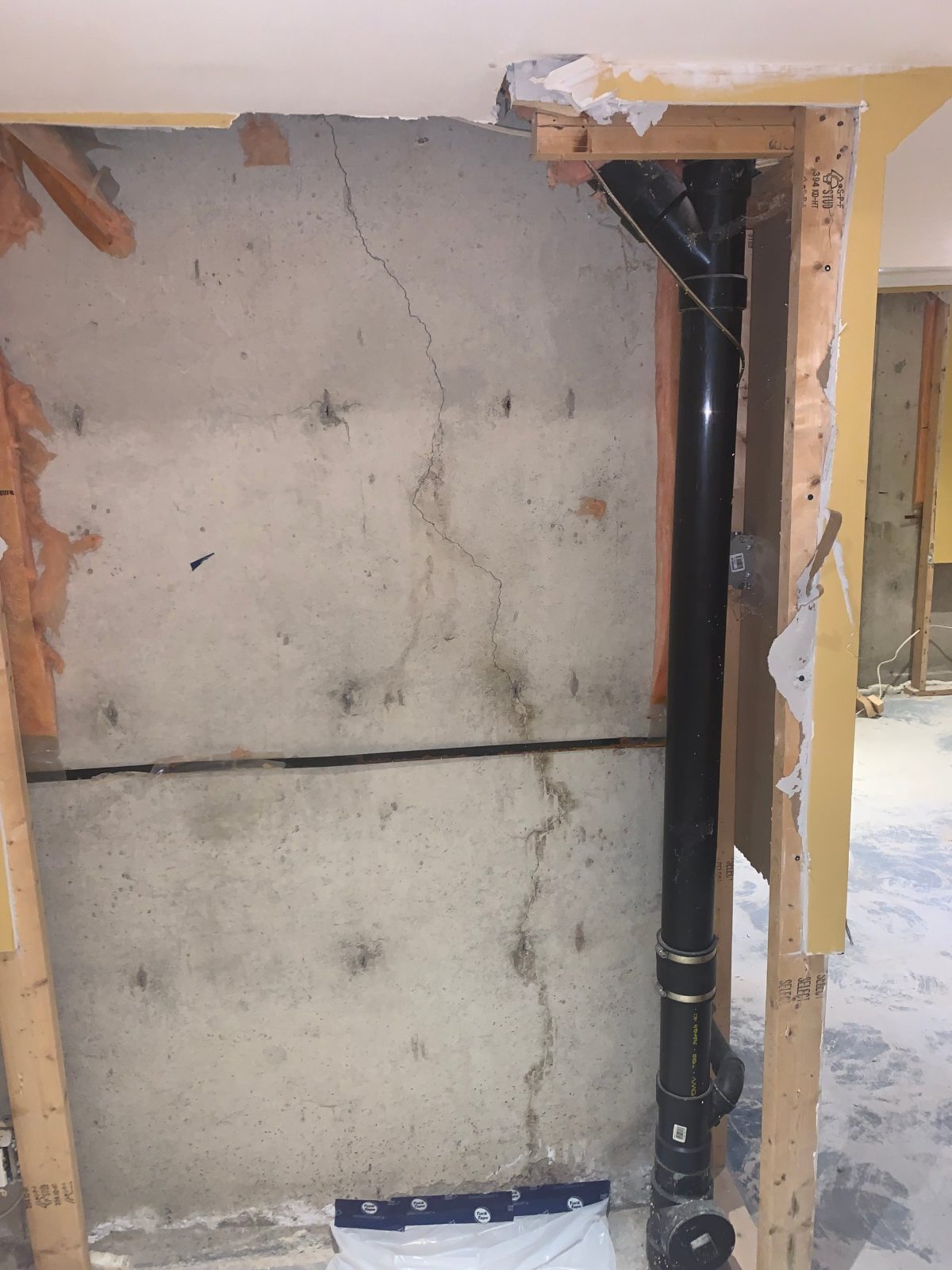 Vertical crack with water staining in a poured concrete basement wall beside a plumbing stack, before crack injection