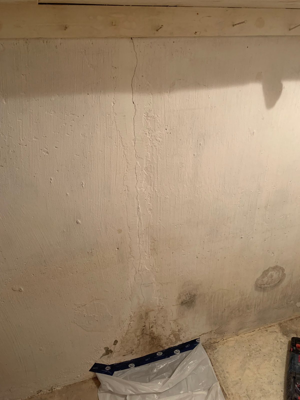 Vertical foundation crack in a painted basement wall with water staining at the base, before crack injection